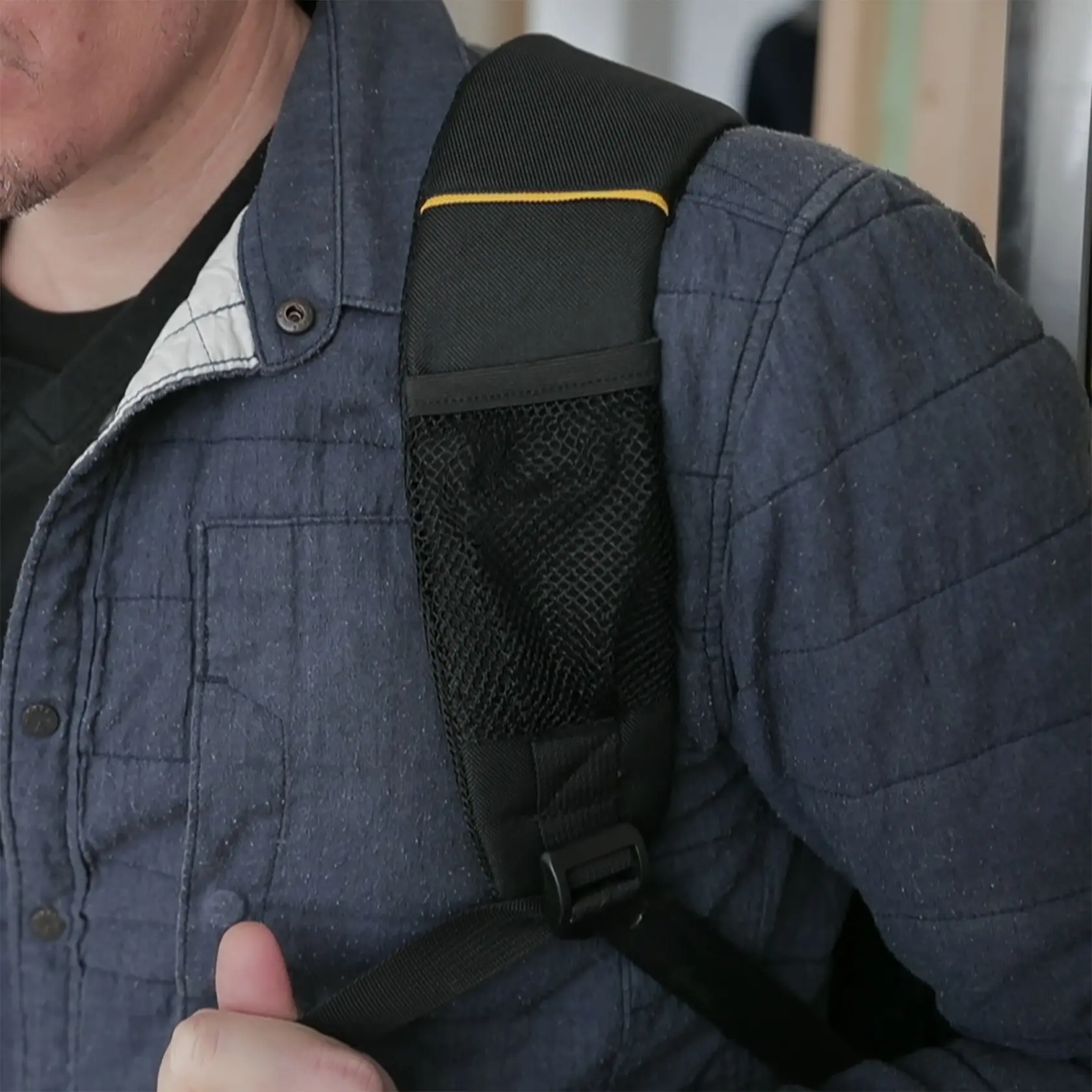 STANLEY 1-95-611 photography of a black backpack strap with mesh pocket and yellow trim on a person's shoulder.