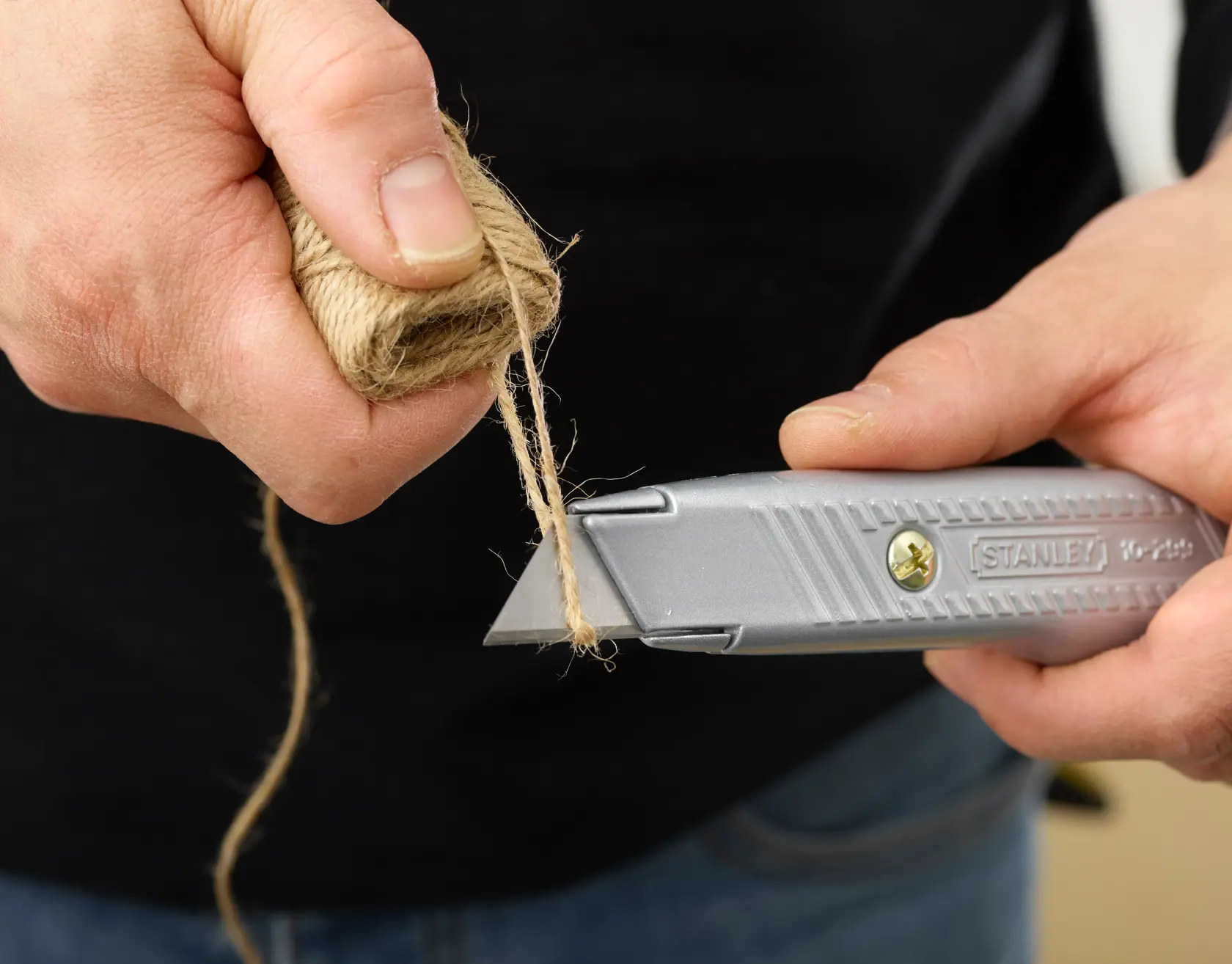 Photo of STANLEY 2-10-199 utility knife cutting twine, close-up of hands and tool in use.