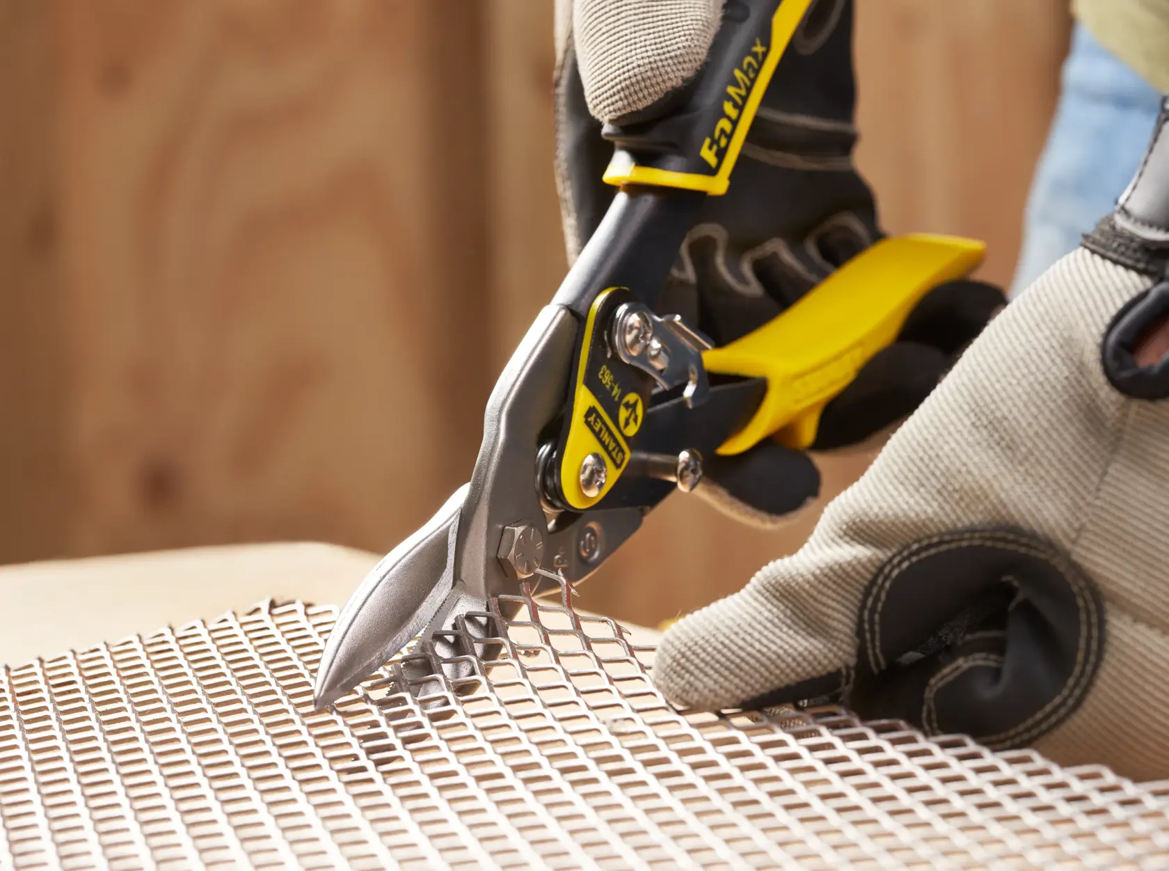 STANLEY 2-14-563 aviation snips cutting metal mesh, close-up with gloved hand holding tool.