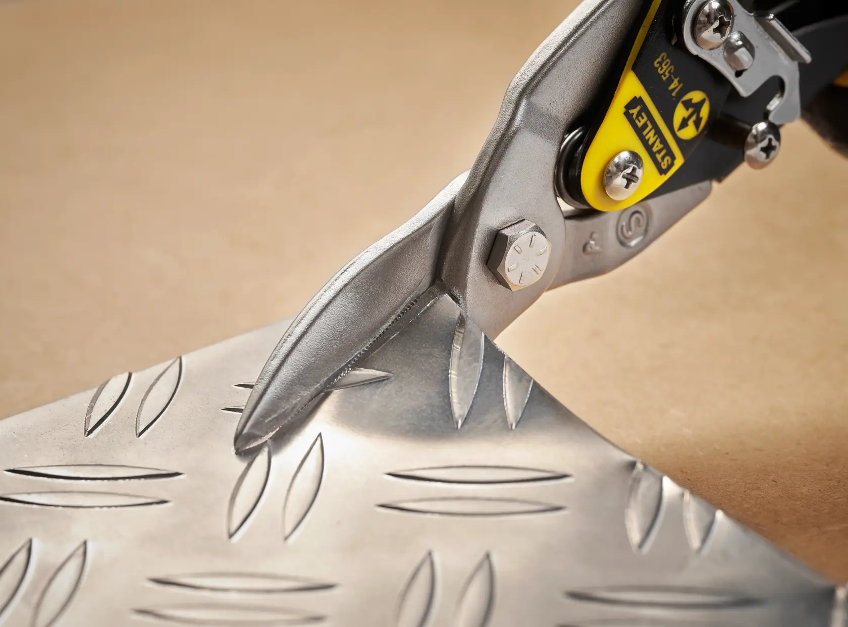 STANLEY 2-14-563 aviation snip cutting patterned metal sheet, close-up angle.