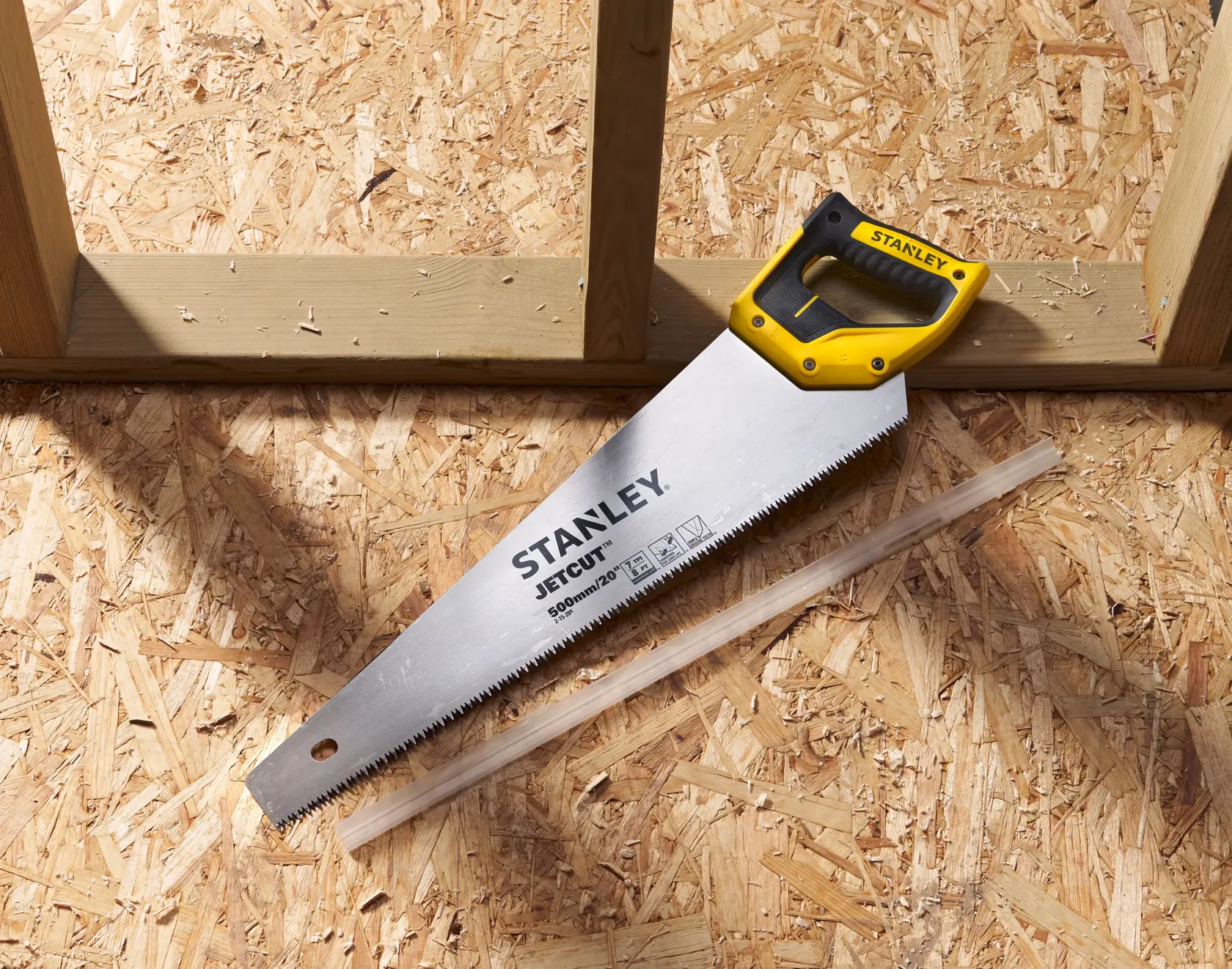STANLEY 2-15-288 hand saw with yellow and black handle on wood panel, top view.