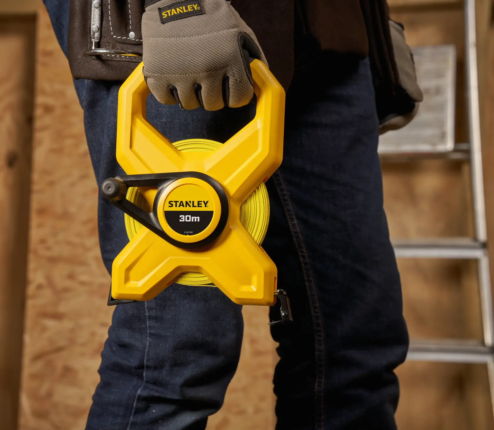 Photo of STANLEY 2-34-792 yellow 30m open reel tape measure held by a worker in gloves, construction setting.