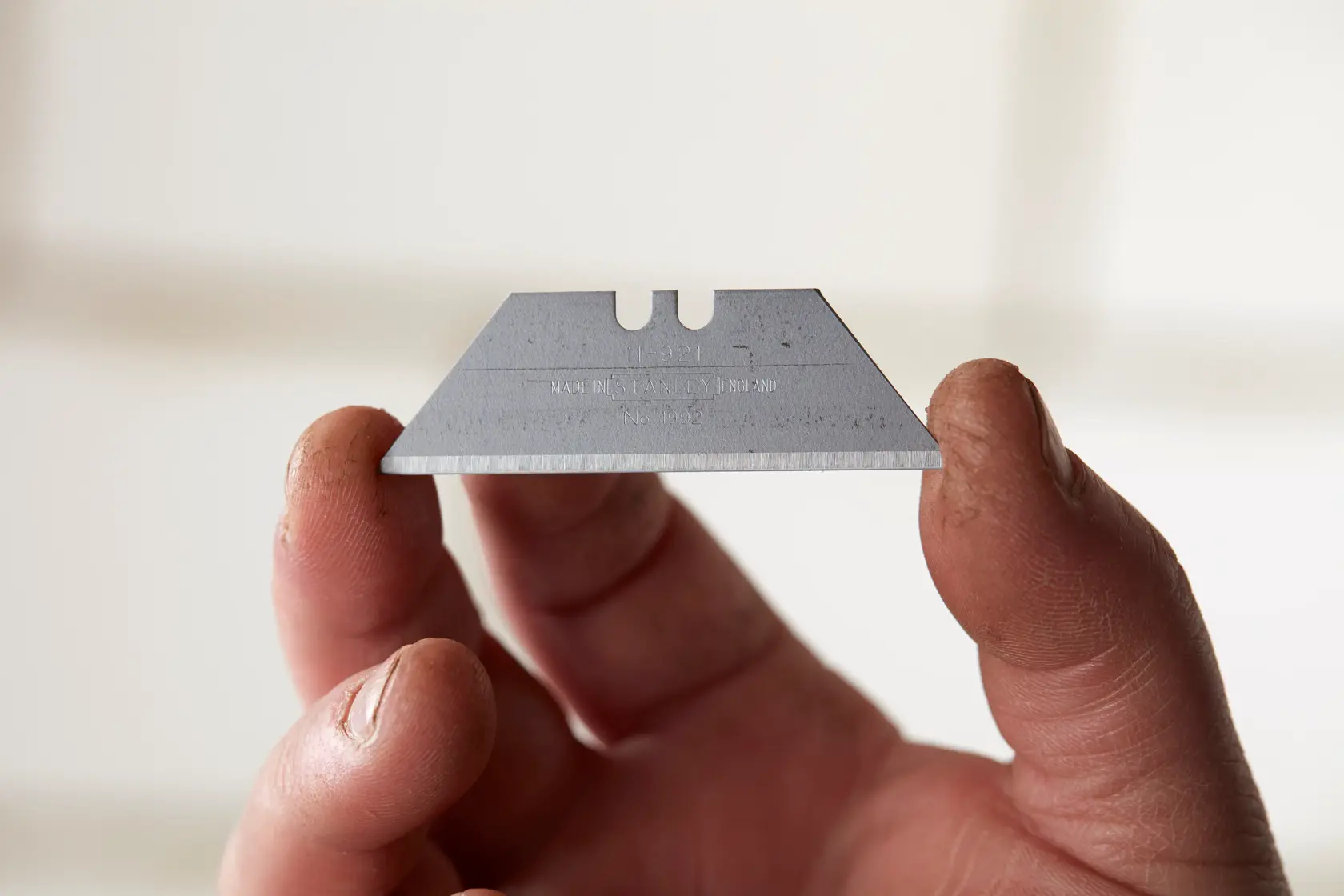Photo of STANLEY 4-11-921 utility blade held between fingers, silver color, sharp edge visible.