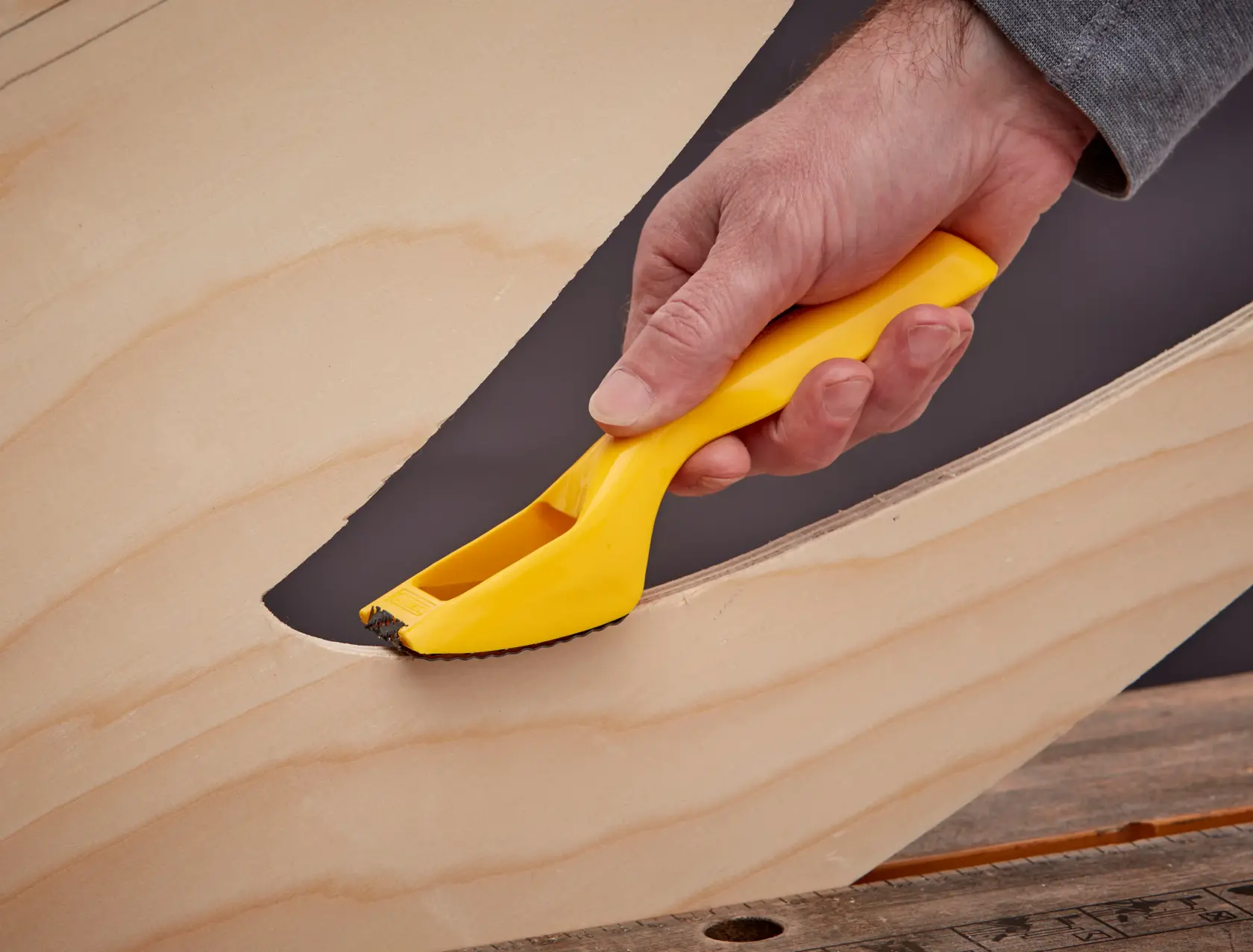 STANLEY 5-21-115 rasp tool with yellow handle smoothing curved wood surface, close-up photo.