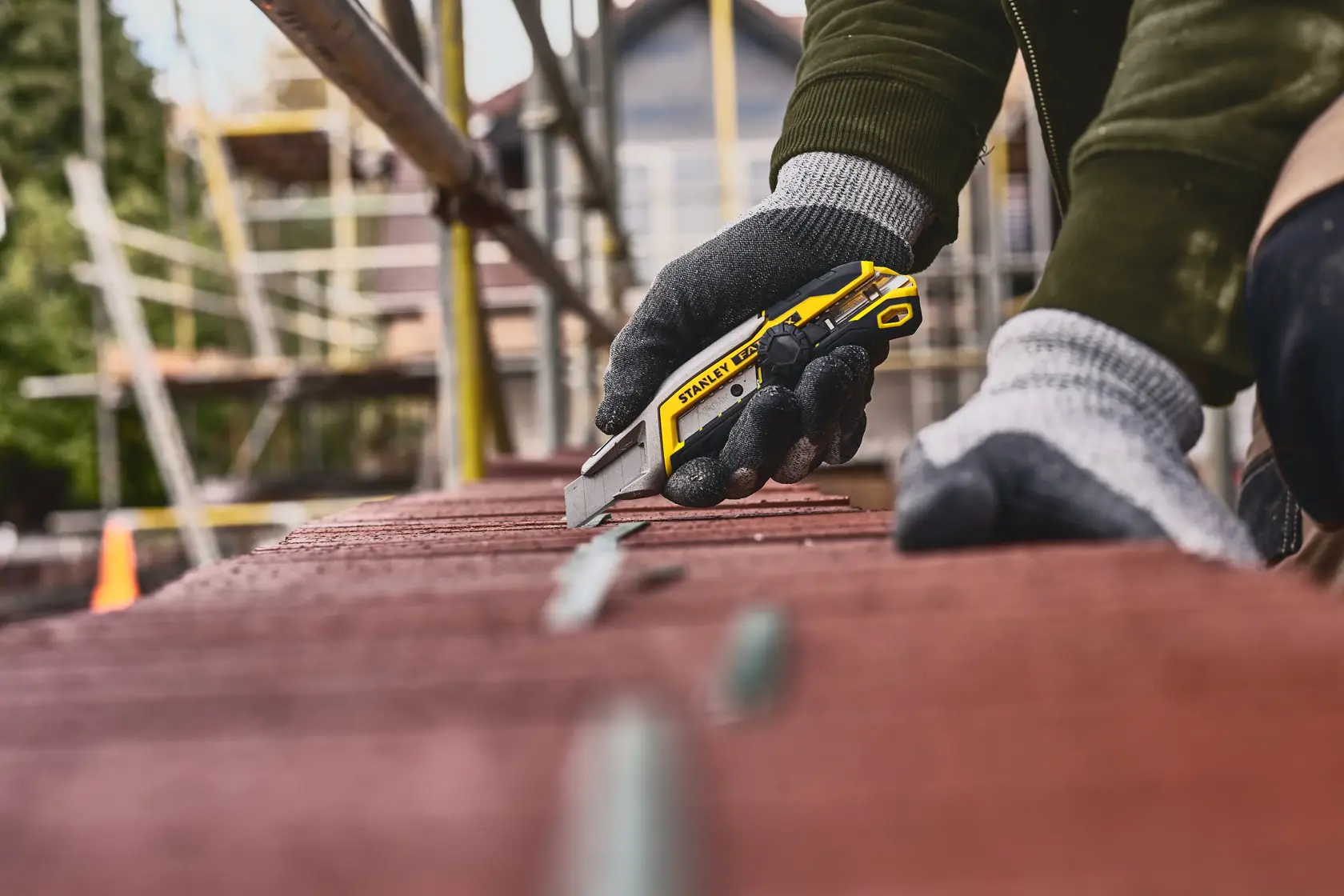 Stanley FMHT10592-0 utility knife in use, yellow and black, held by gloved hand on construction site.