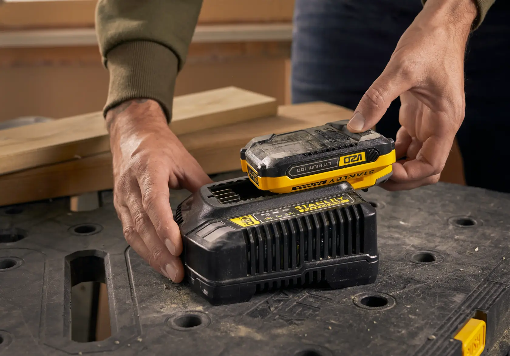 Photo of STANLEY SFMCB14 battery charger with battery on workbench, hands placing battery onto charger.