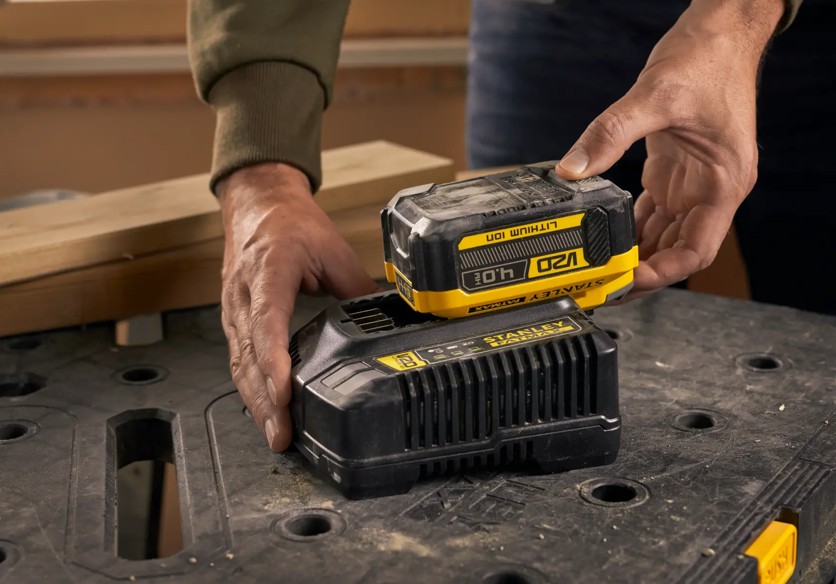 Photo of STANLEY SFMCB204 battery being placed on charger on workshop table.