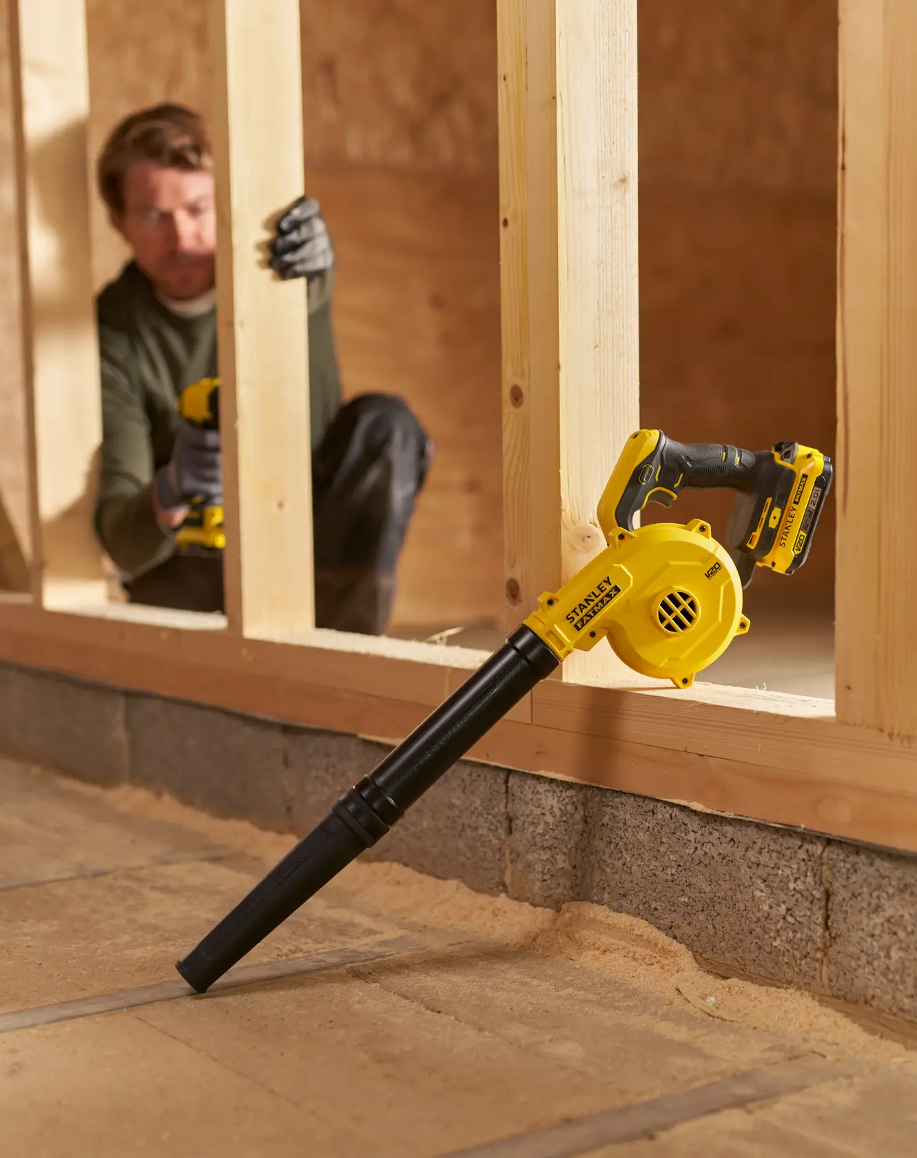 STANLEY SFMCBL01B cordless blower resting on wood frame, yellow and black design, indoor construction setting.