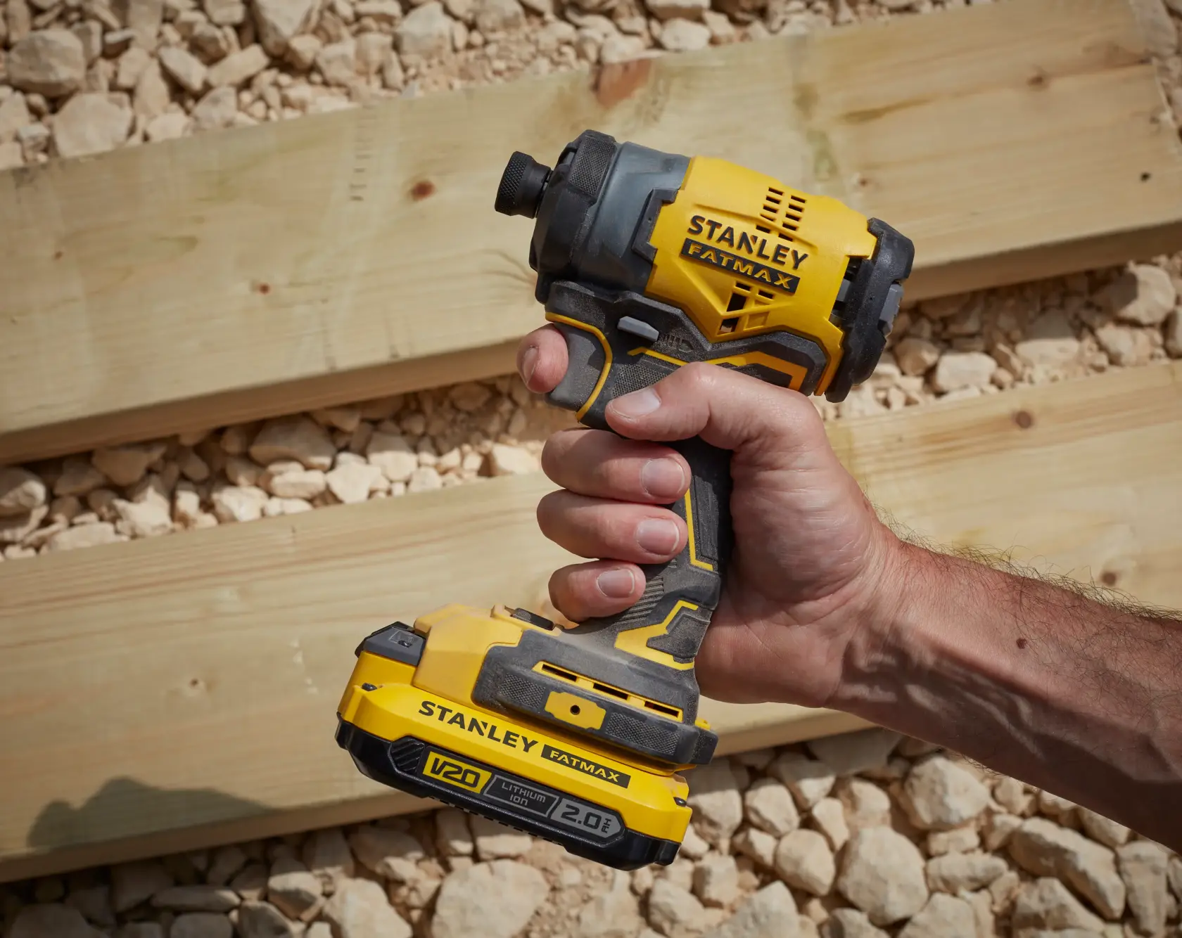 STANLEY SFMCF810B cordless impact driver held in hand, yellow black, used near wooden planks outdoors.