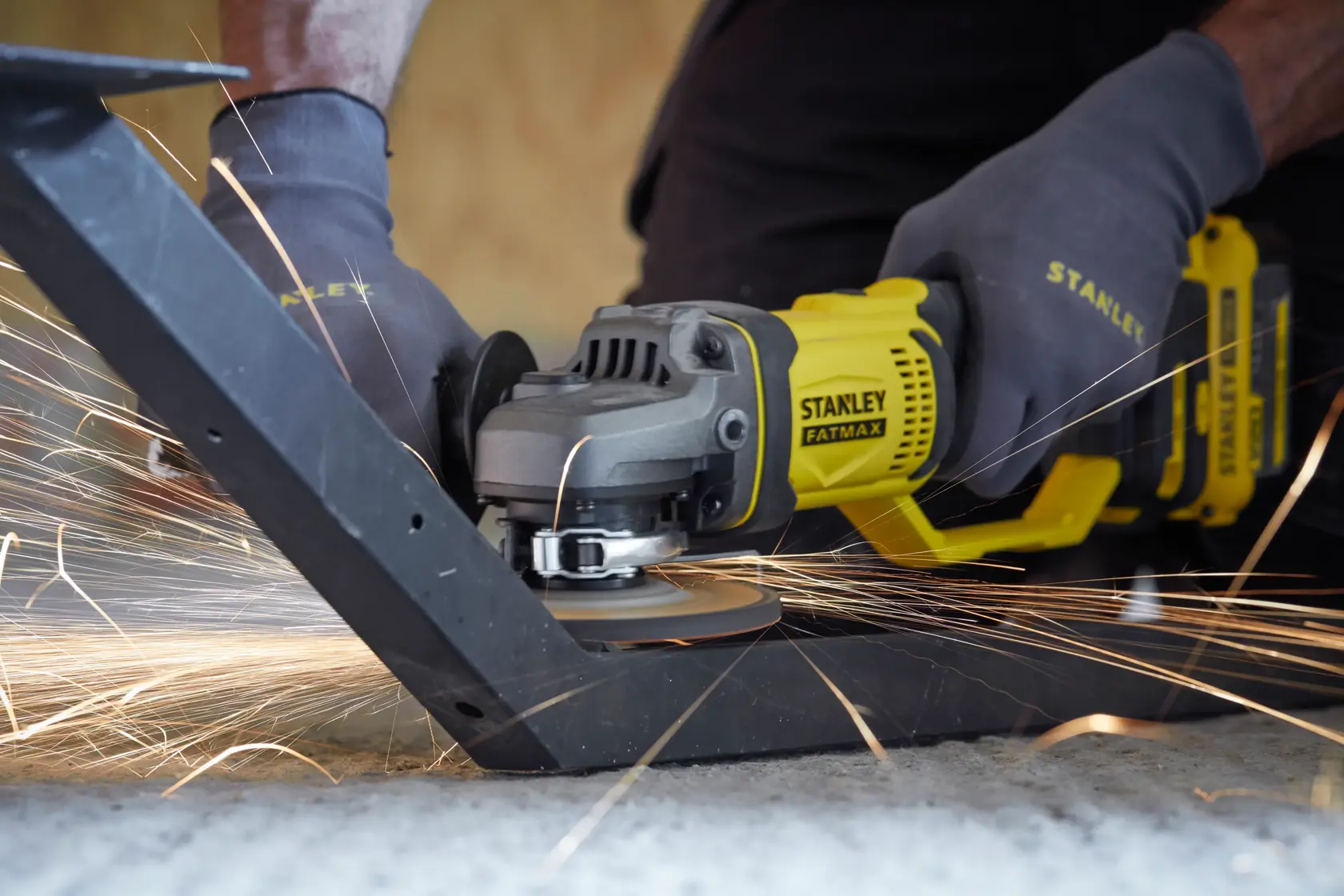 STANLEY SFMCG400M2K angle grinder in use on metal, close-up with sparks flying, user wearing gloves.