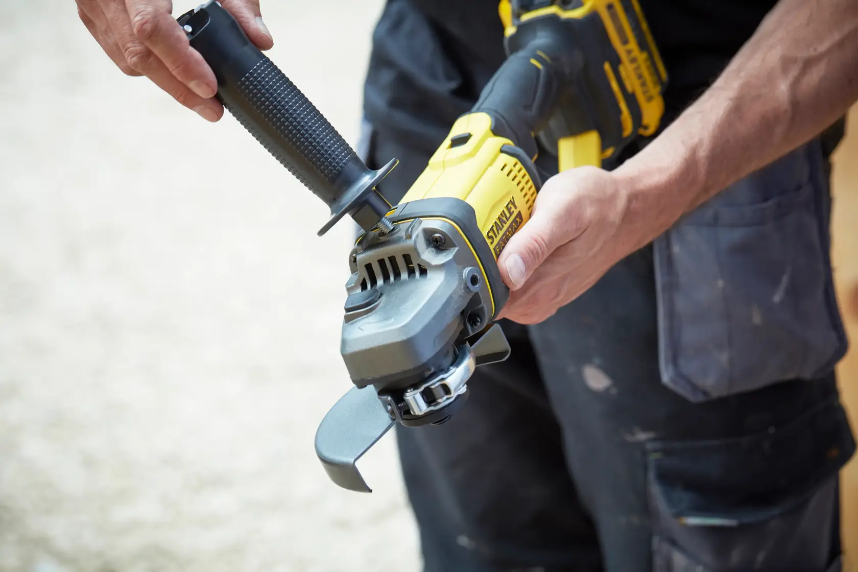 STANLEY SFMCG400M2K angle grinder held in hands, yellow and black body, being assembled outdoors.