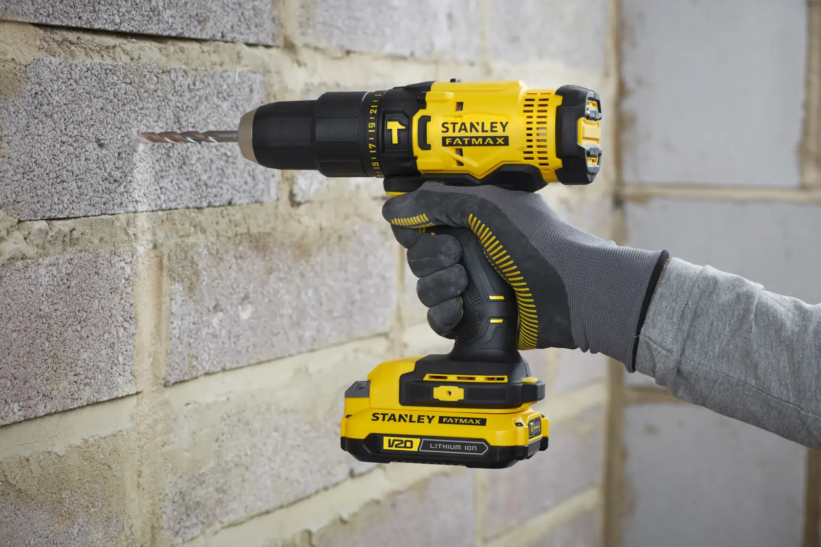 STANLEY SFMCK465D2S cordless drill driver in use drilling into a brick wall, close-up side view.