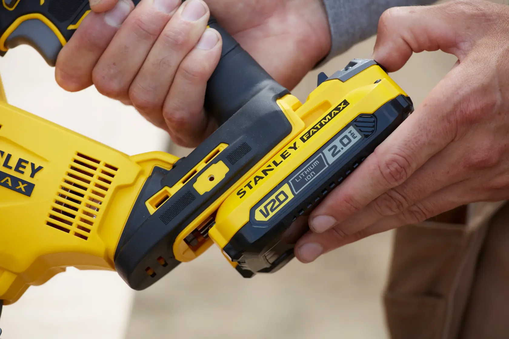 Close-up of hands attaching a STANLEY FATMAX V20 Lithium-Ion battery to a yellow power tool.