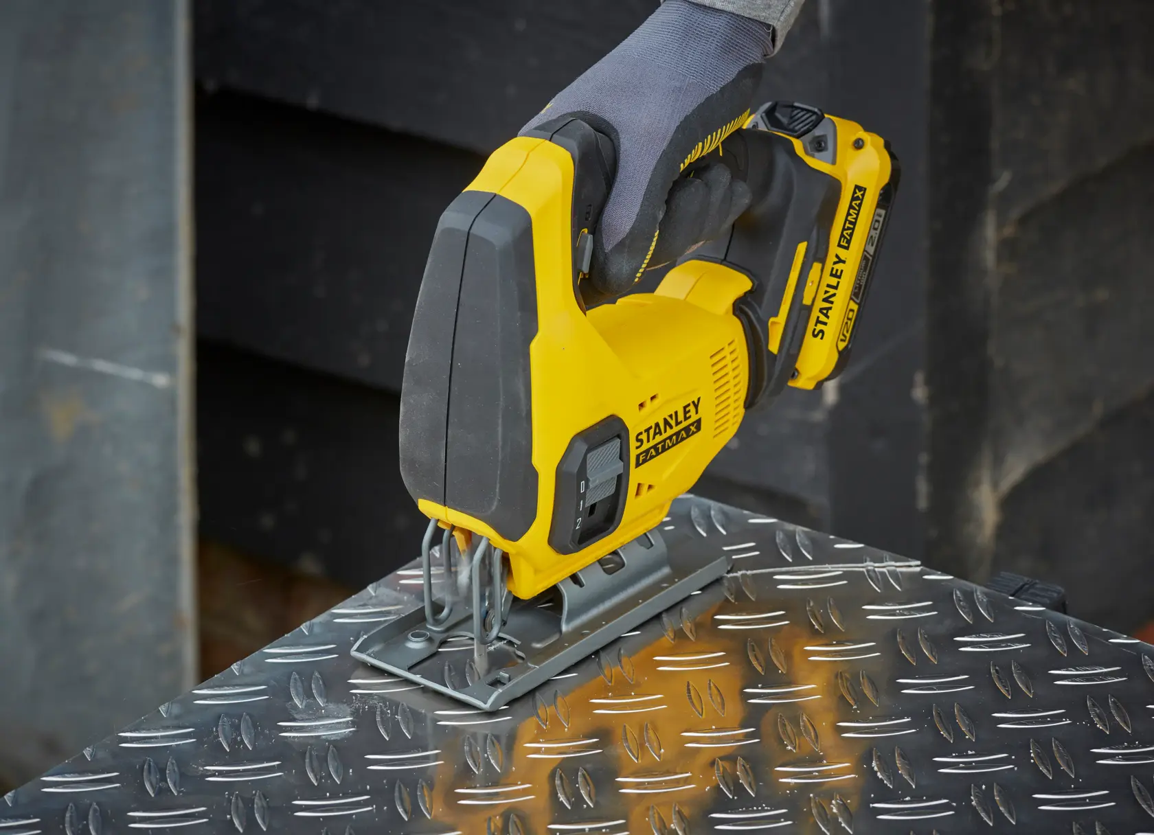 STANLEY cordless jigsaw cutting metal, operated by a gloved hand. Bright yellow tool for precision work.