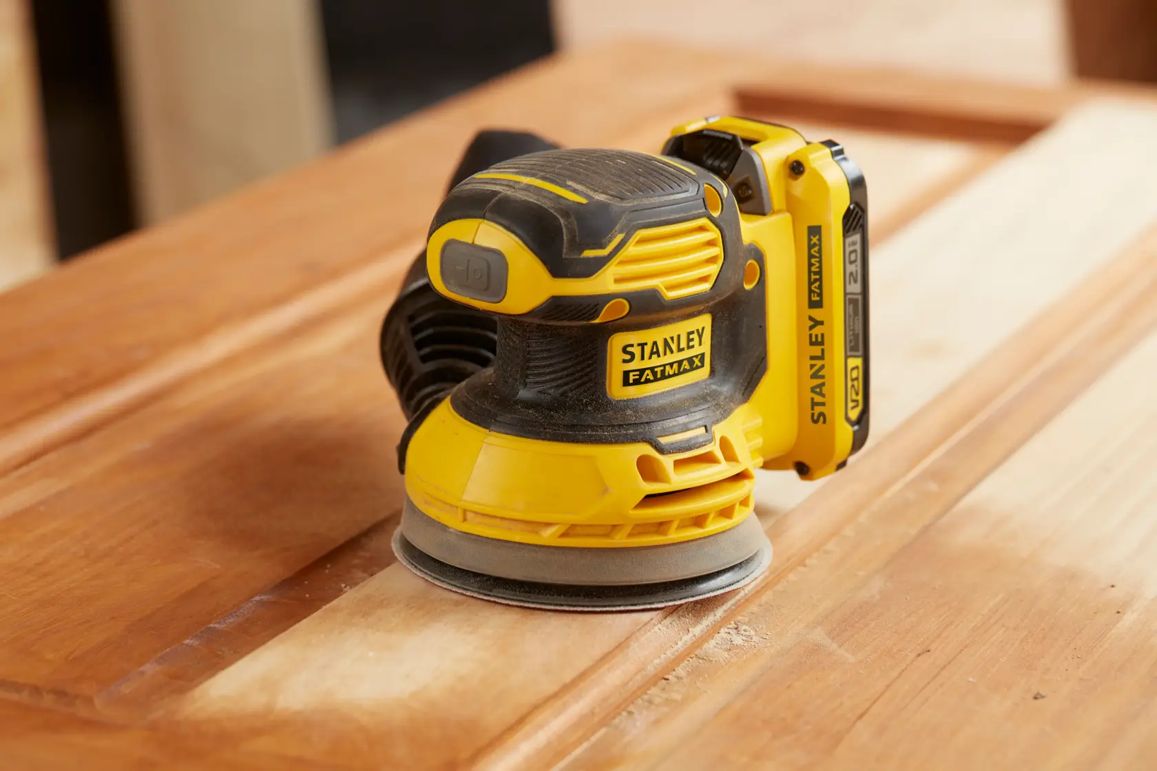 STANLEY SFMCW220B cordless sander on wooden surface, yellow and black, close-up side angle.