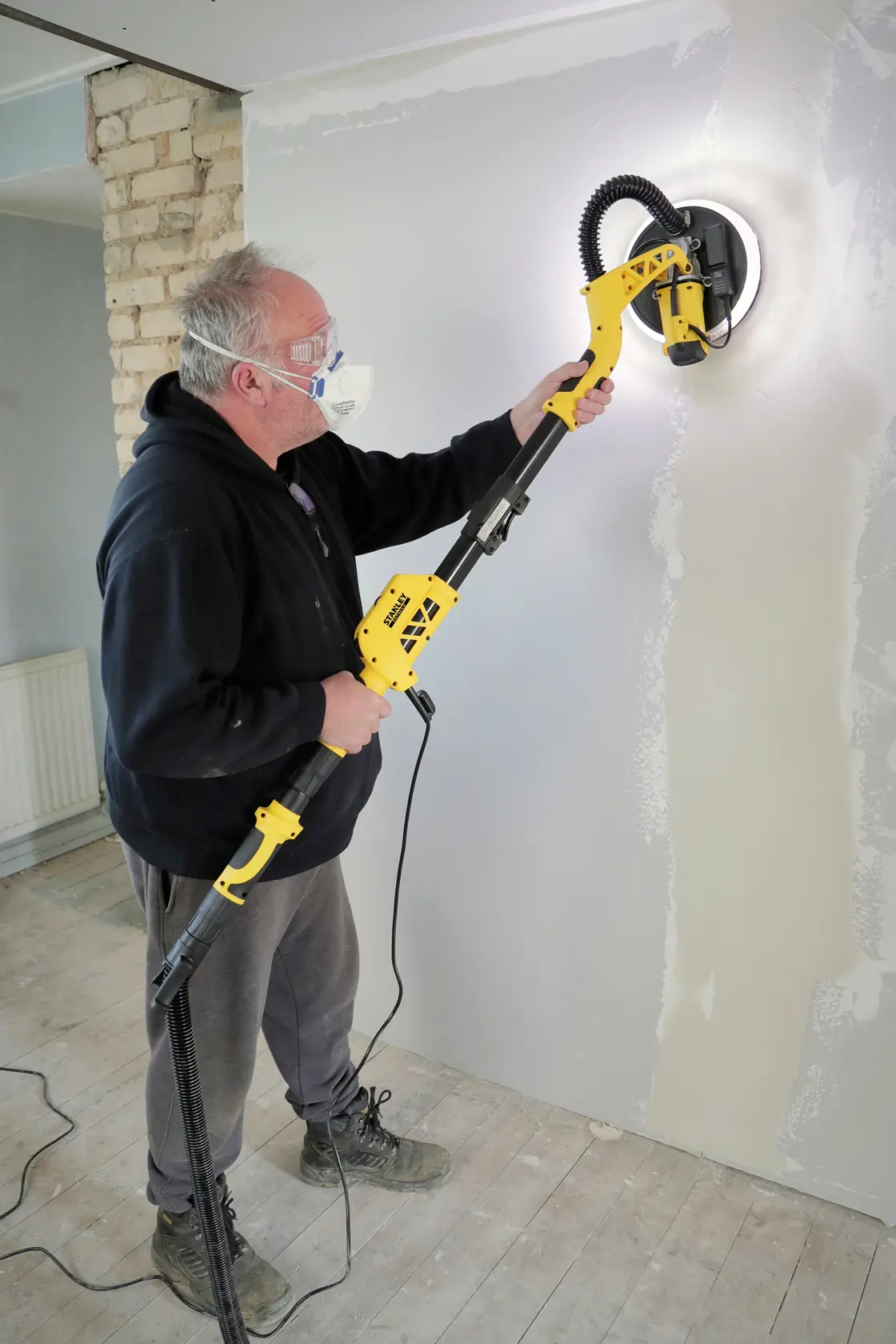 STANLEY SFMEE500S drywall sander in use on a wall, shown from the side indoors.