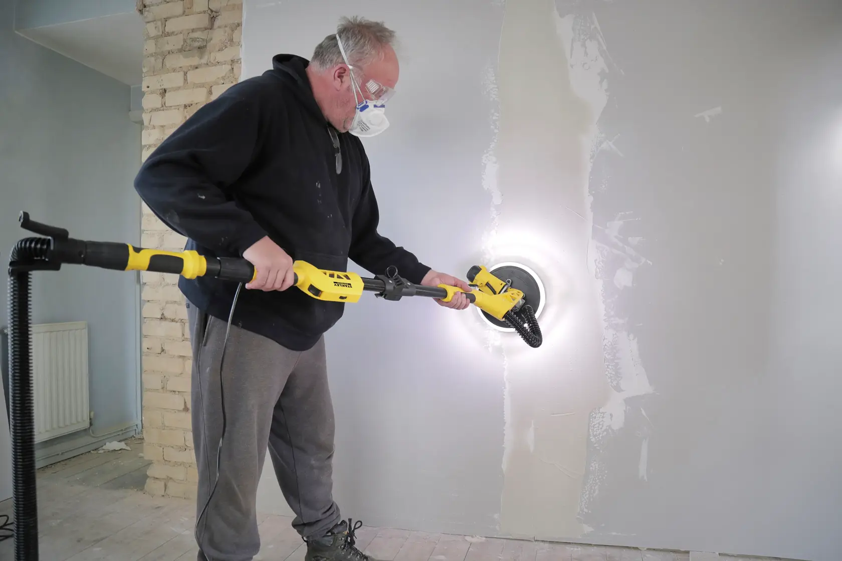 Photo of STANLEY SFMEE500S drywall sander in use on a wall during renovation, side angle view.
