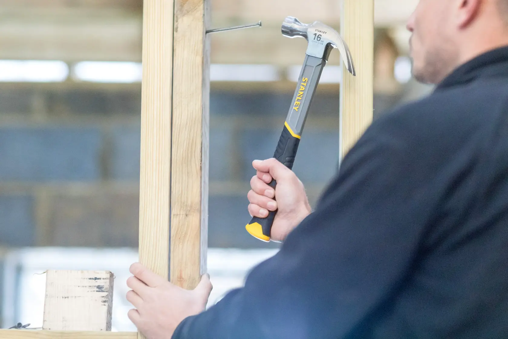 Photo of STANLEY STHT0-51309 claw hammer striking a nail into wooden frame, tool held by a person.