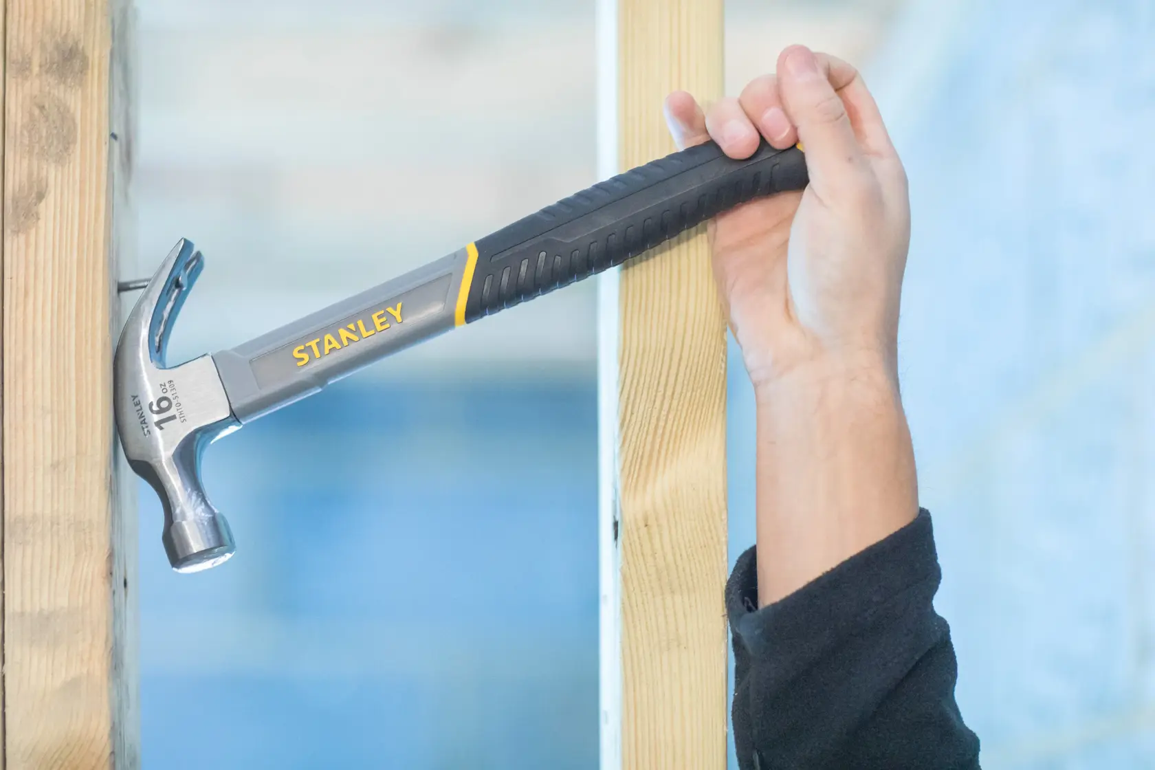 Stanley STHT0-51309 claw hammer with black grip, held against wooden beam, close-up photography.