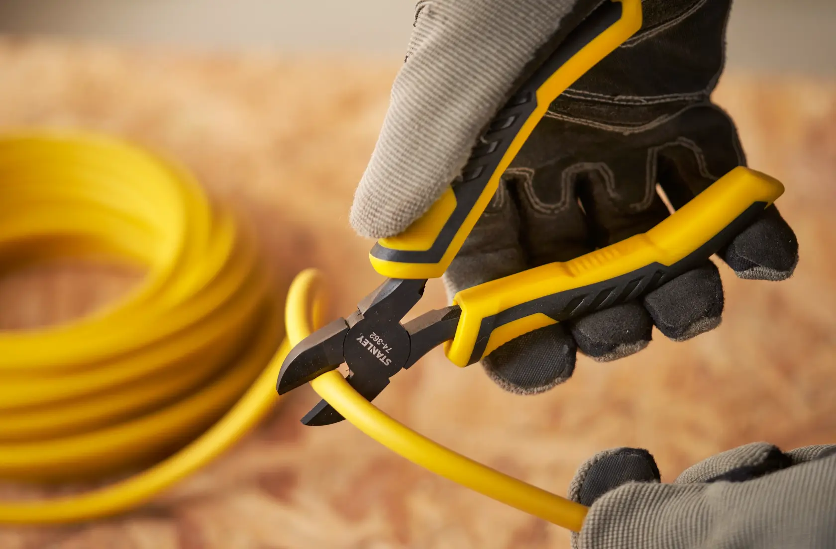 STANLEY STHT0-74362 pliers cutting yellow cable, close-up photography, person wearing gloves.
