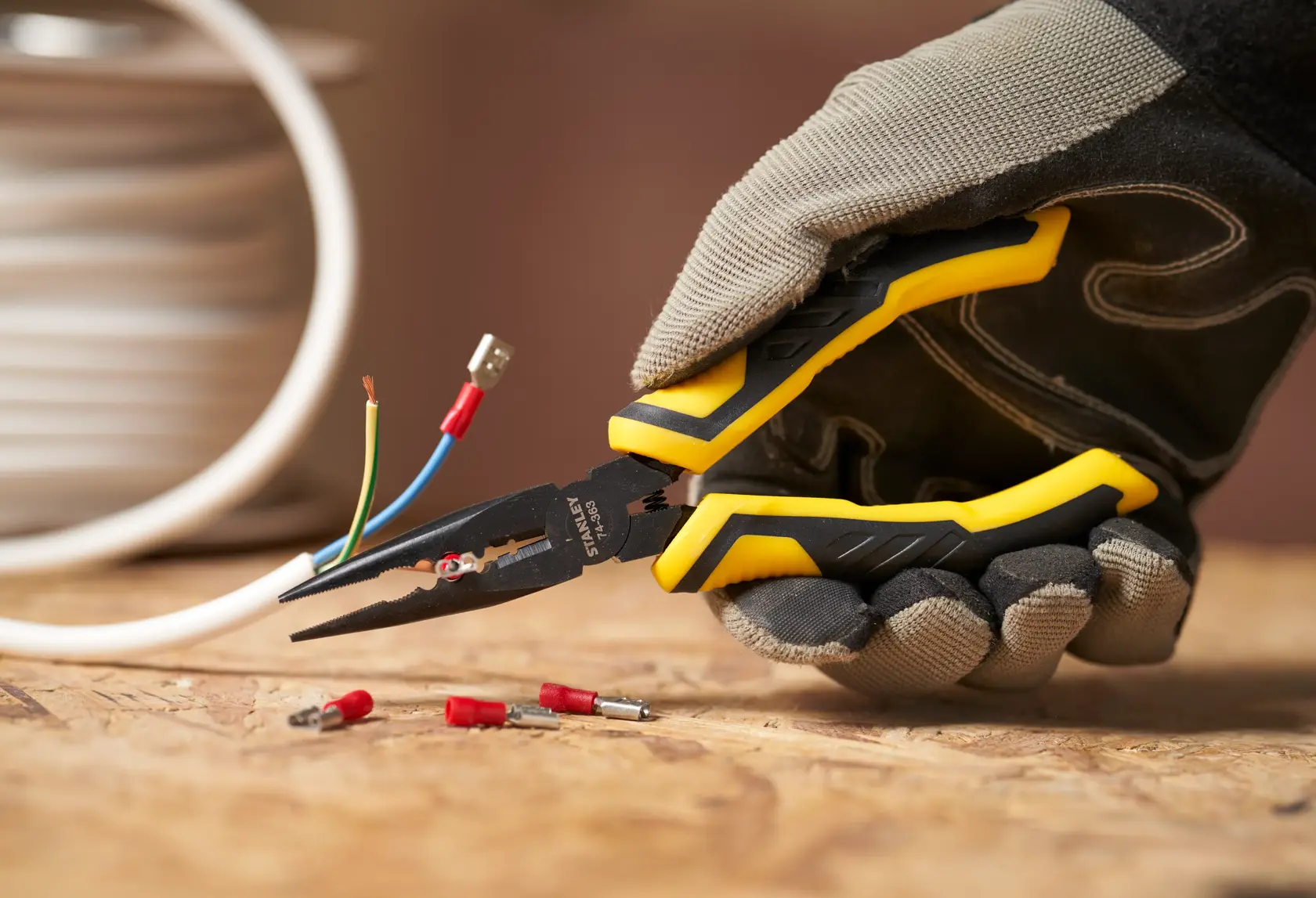 STANLEY STHT0-74364 pliers with yellow and black handles held by gloved hand, gripping electrical wire.