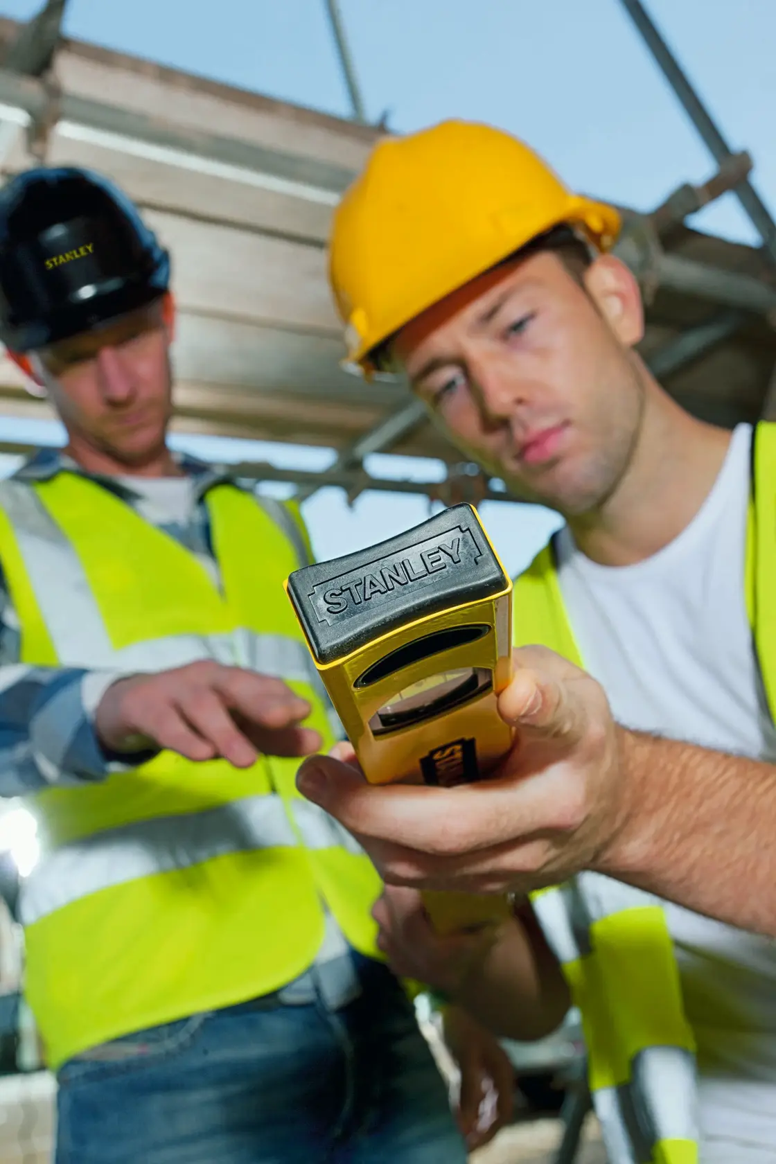STANLEY STHT1-43102 spirit level held by workers in safety vests and helmets at construction site.