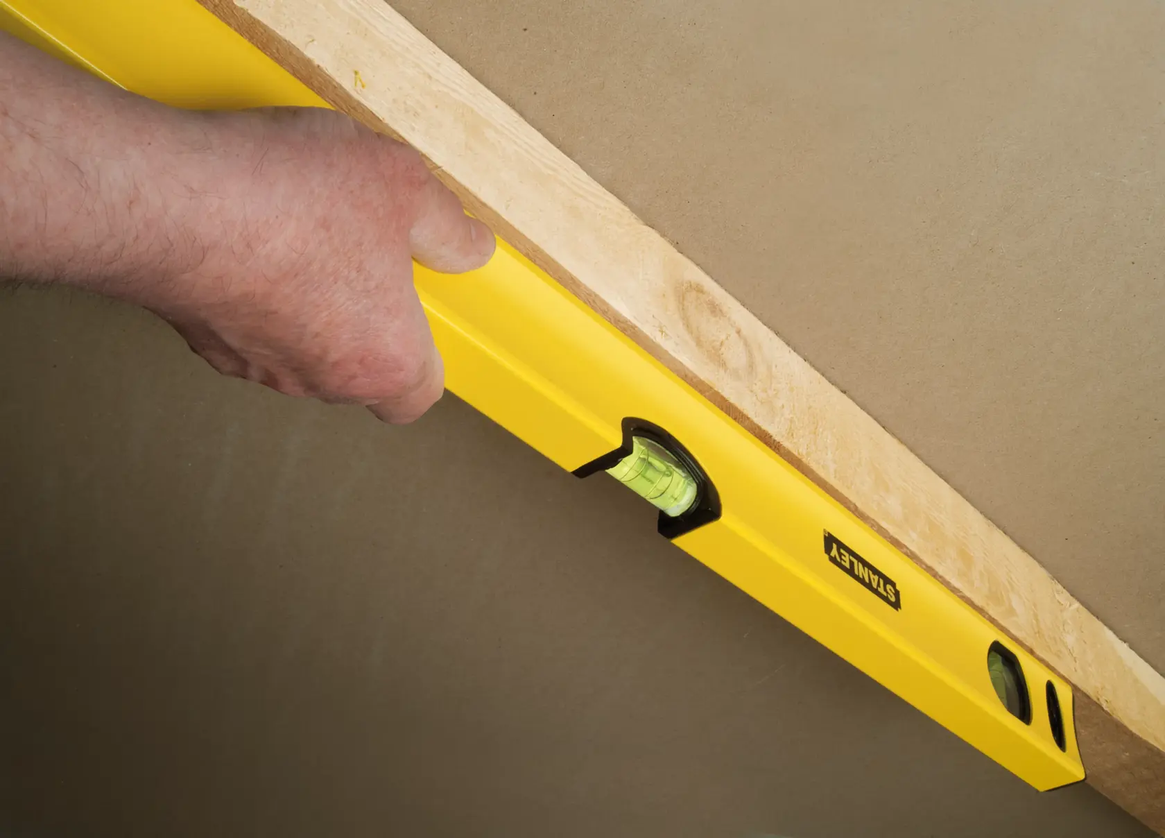 STANLEY STHT1-43103 yellow spirit level held against wood, side view, used for precise leveling.