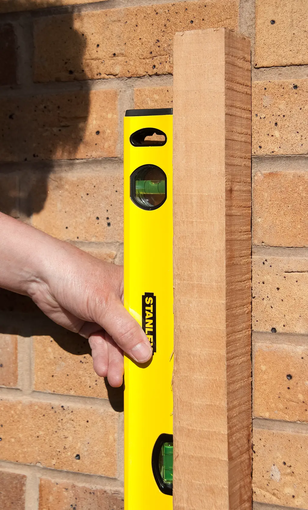STANLEY STHT1-43103 yellow spirit level held against wood and brick wall, close-up view.