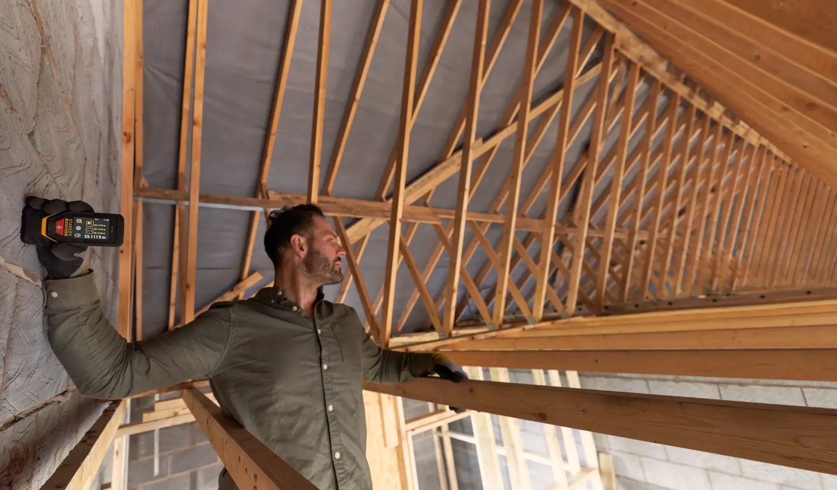 Person using STANLEY STHT1-77140 laser distance measurer inside wooden roof construction.