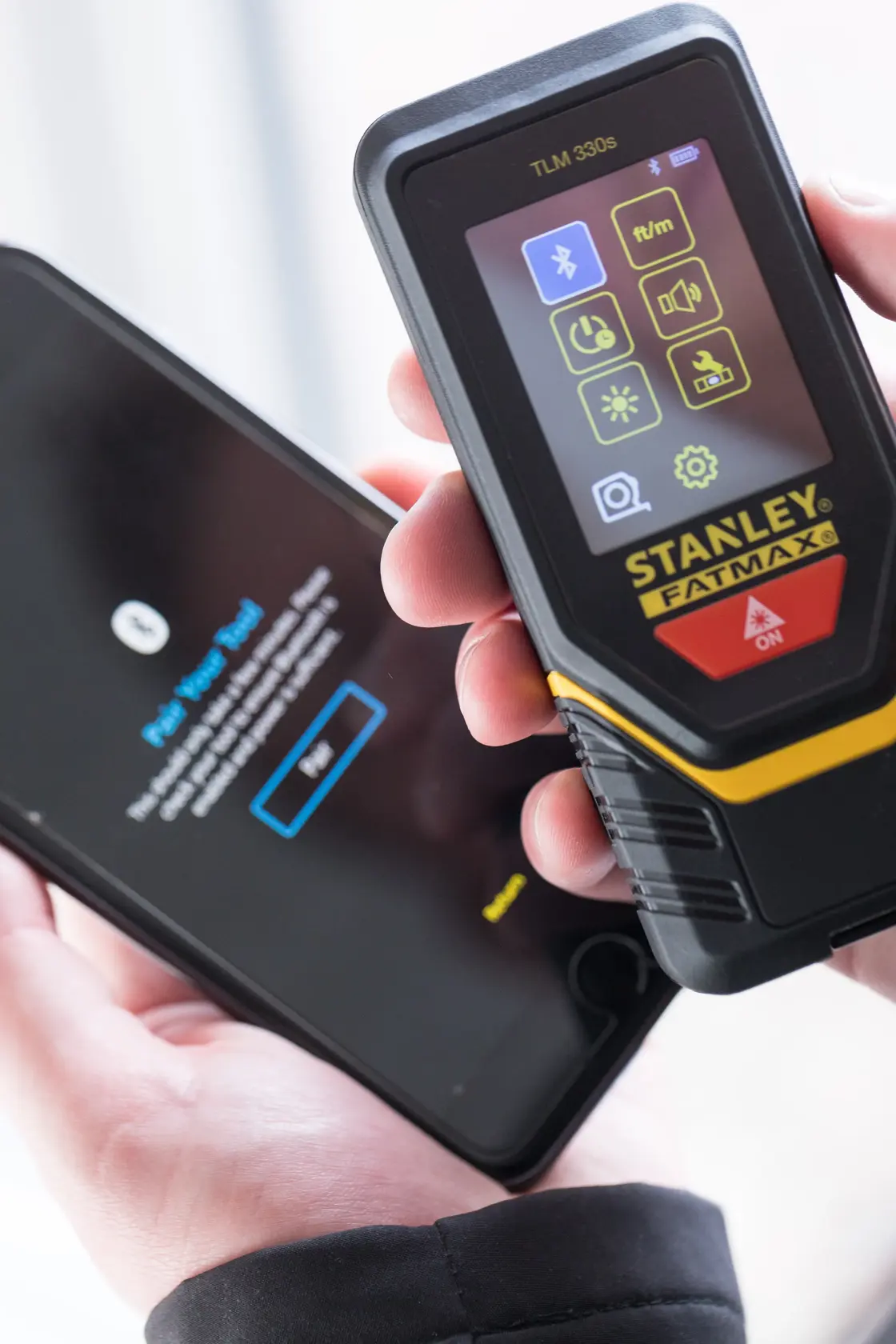 STANLEY STHT1-77140 laser distance measurer held near smartphone, close-up front view.