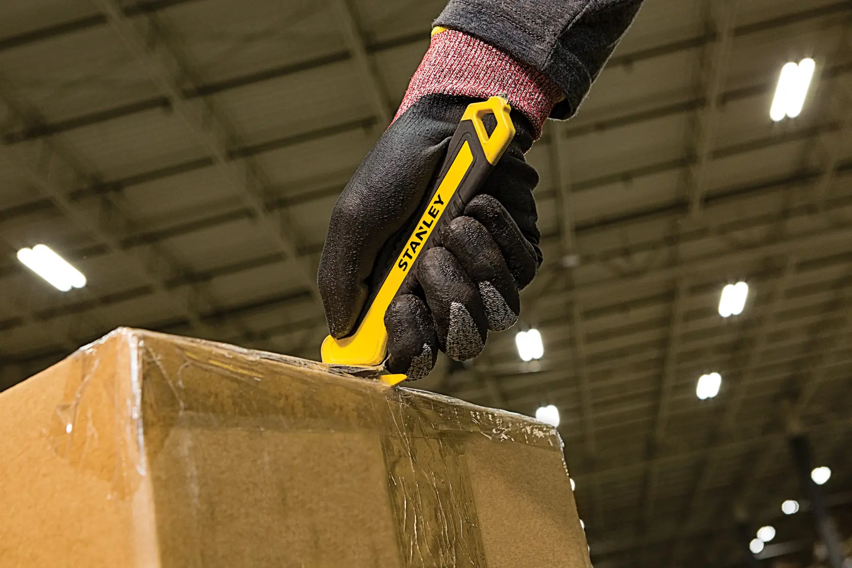 STANLEY STHT10356-0 utility knife cutting tape on a cardboard box in a warehouse setting.