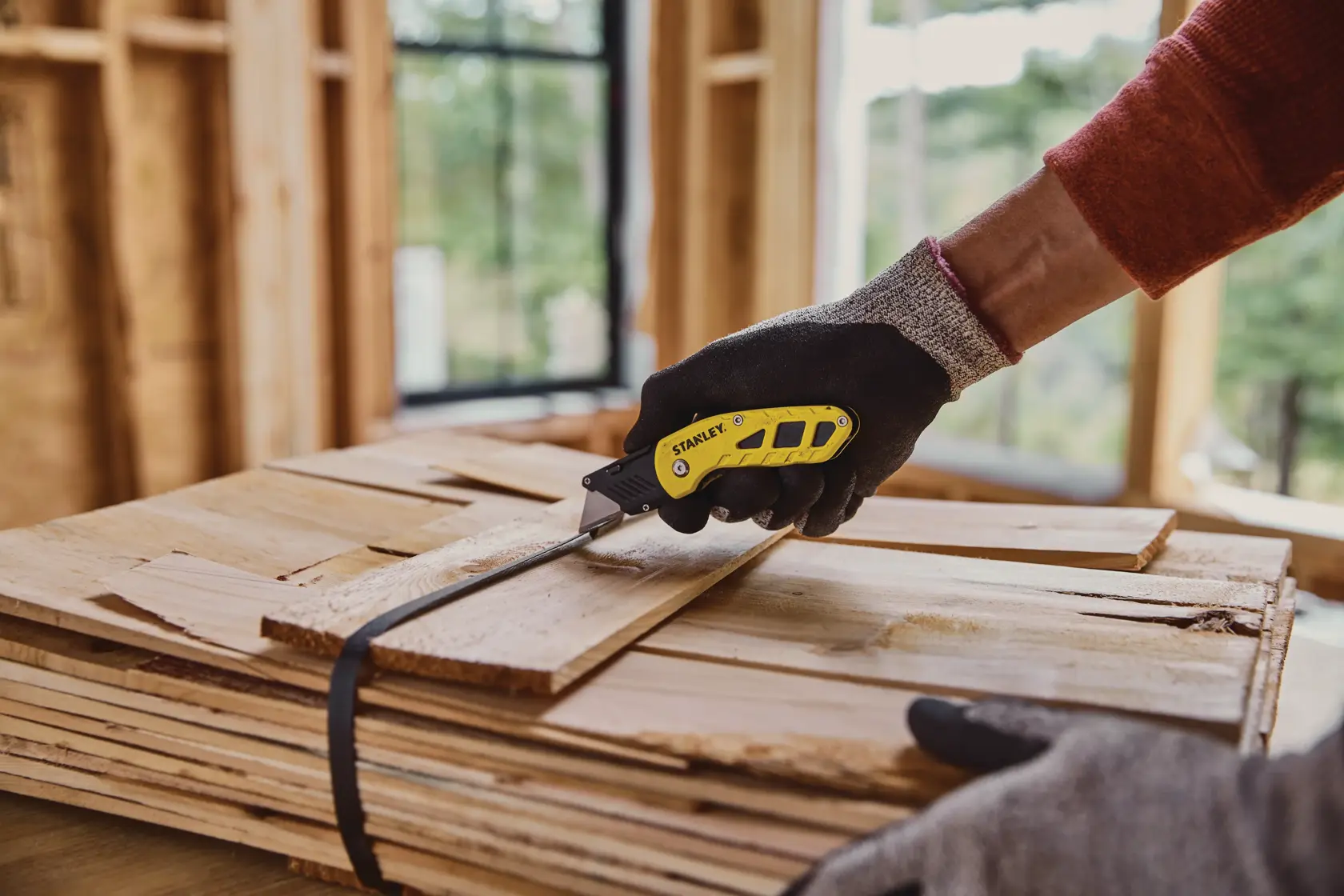Photo of STANLEY STHT10424-0 folding utility knife cutting wood strap in construction setting.