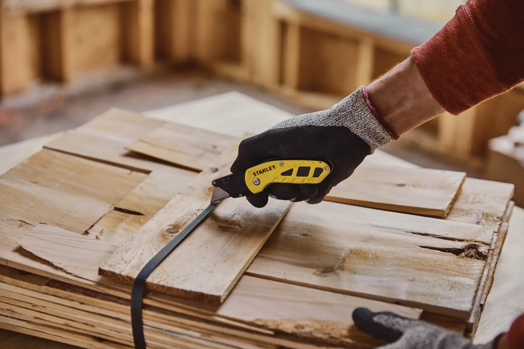 STANLEY STHT10424-0 folding utility knife cutting black strap on stacked wood, close-up view.