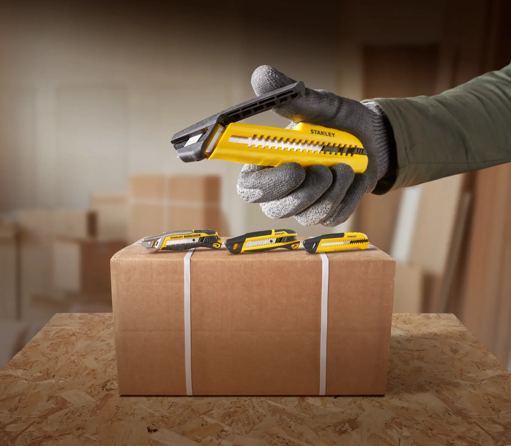 Photo of STANLEY STHT10489 utility knife with yellow and black body beside cardboard box in workshop setting.