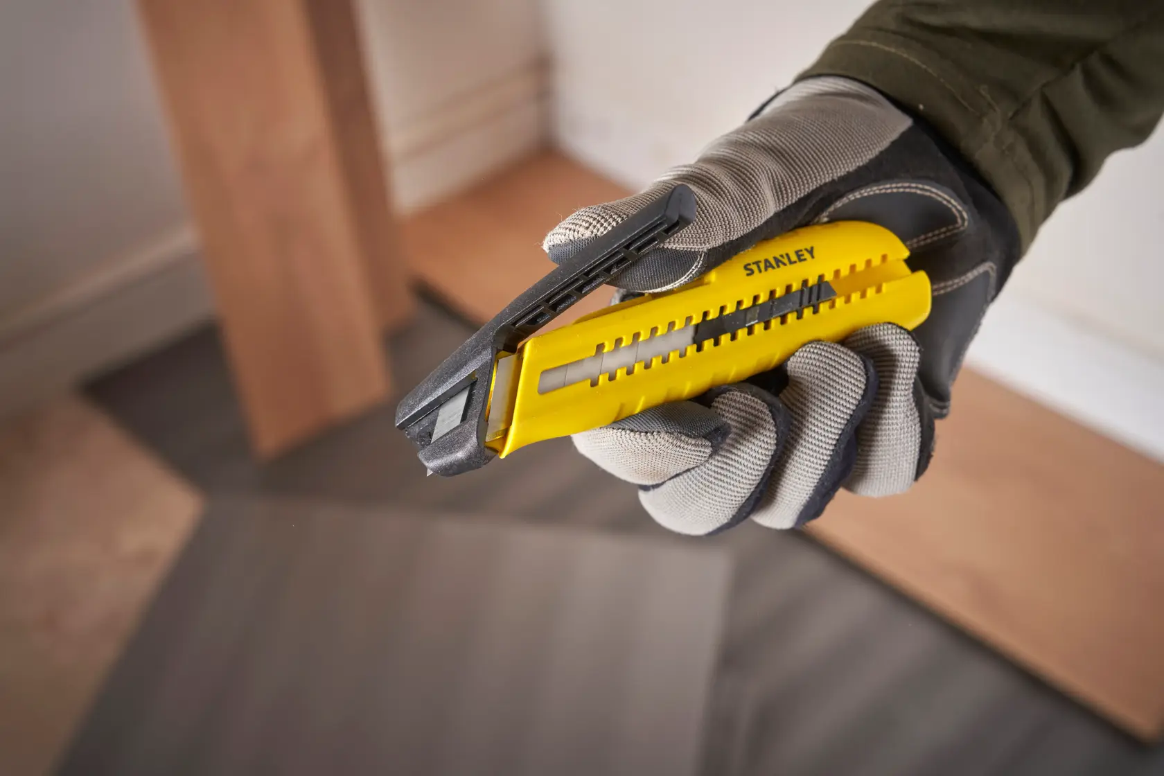 STANLEY STHT10489 utility knife with yellow and black handle, gloved hand holding tool, angled view.