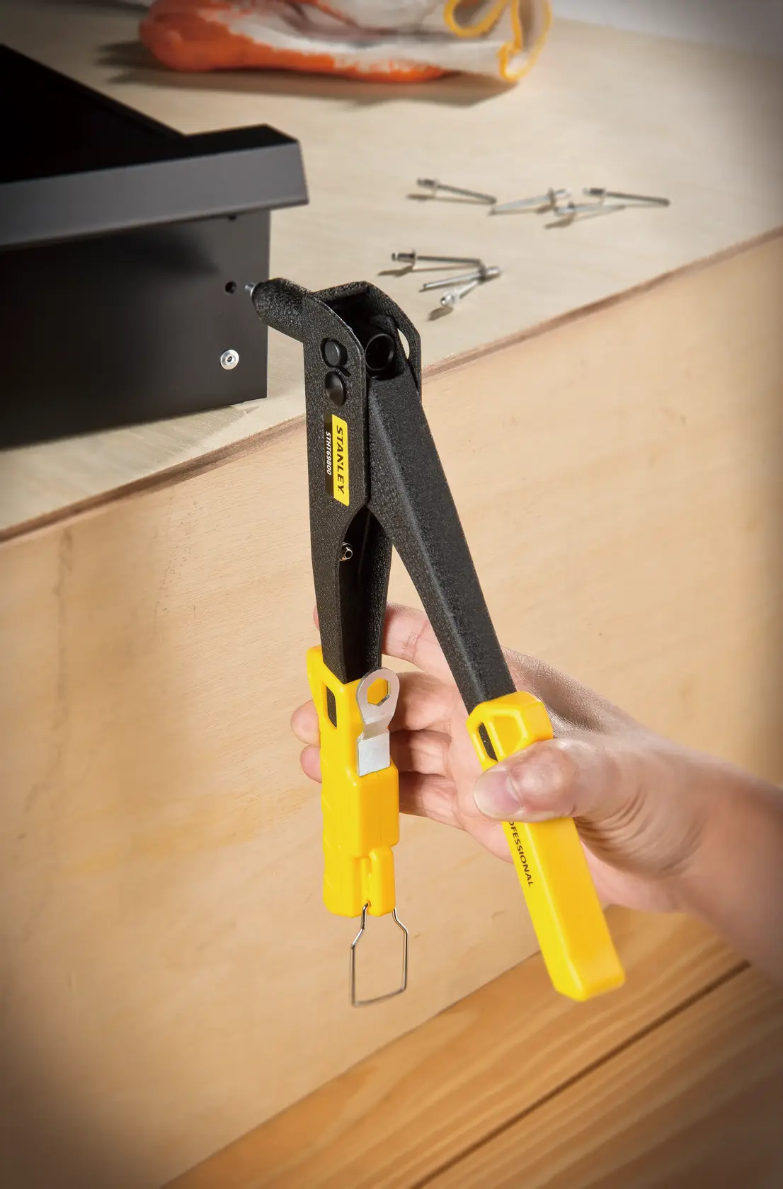 STANLEY STHT69800-8 riveter tool with yellow handles in use, fastening metal to wood, close-up angle.