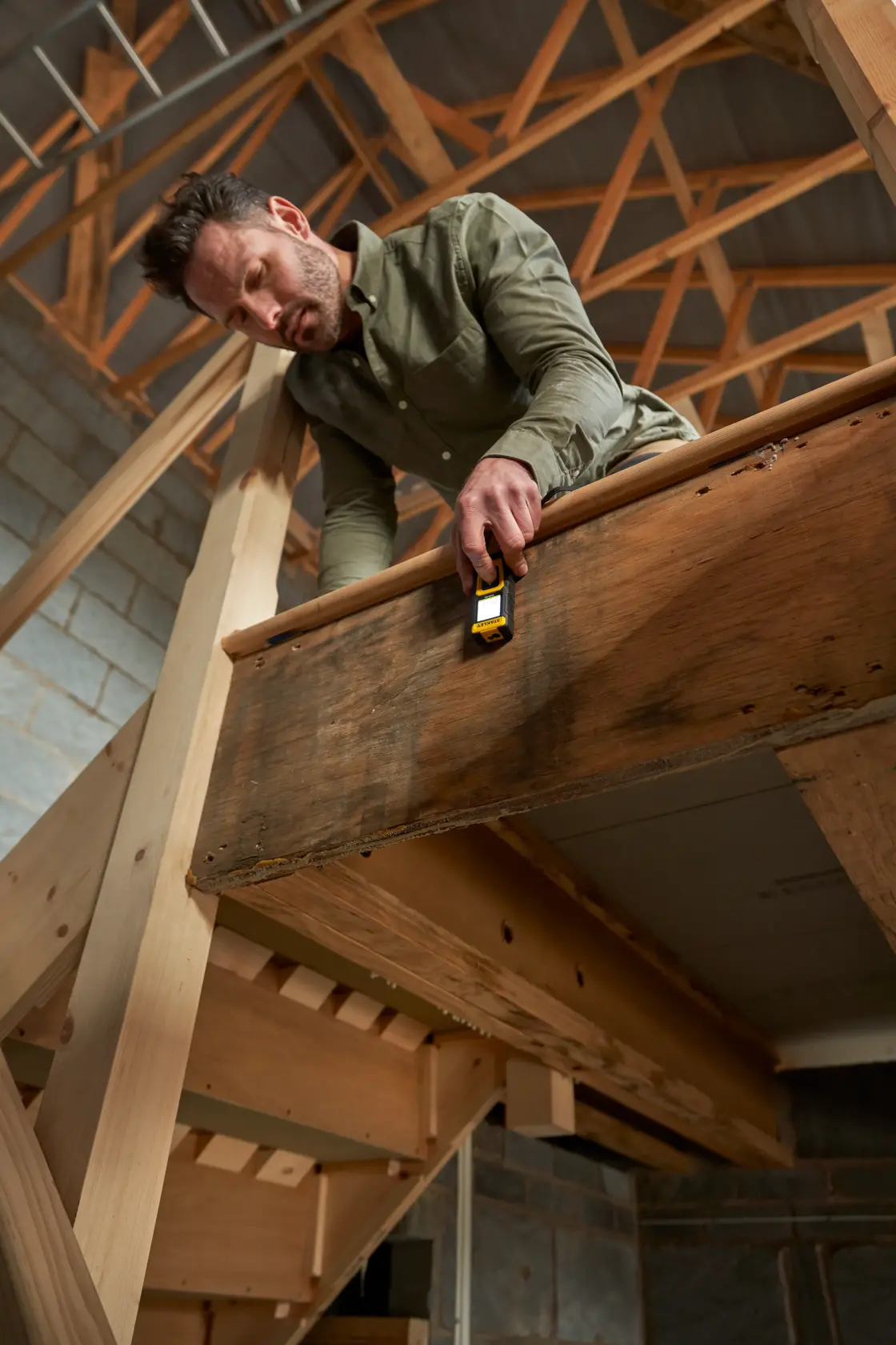 Photo of STANLEY STHT77100-0 laser distance measurer in use on a wooden stair rail in a construction setting.