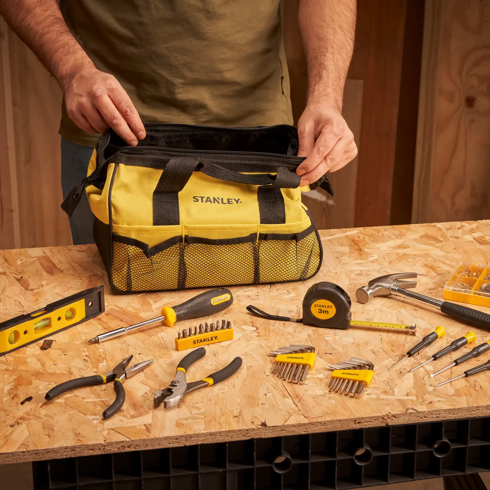 STANLEY STMT0-74101 tool bag in yellow with black accents, surrounded by hand tools on a workbench.