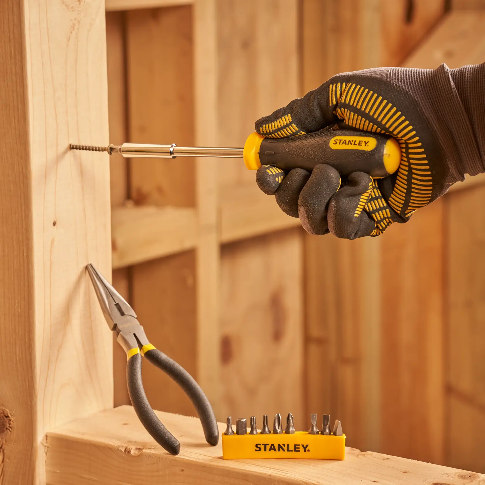 Photo of STANLEY STMT0-74101 screwdriver set with yellow handle used on wood, bit set and pliers visible.