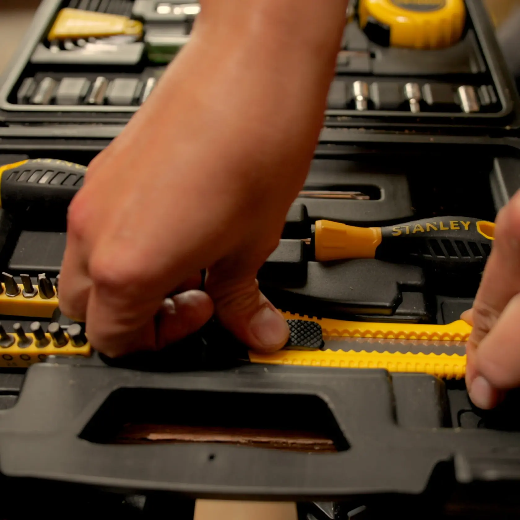 Photo of STANLEY STMT0-74864 tool set with hands selecting yellow cutter and screwdriver from black case.