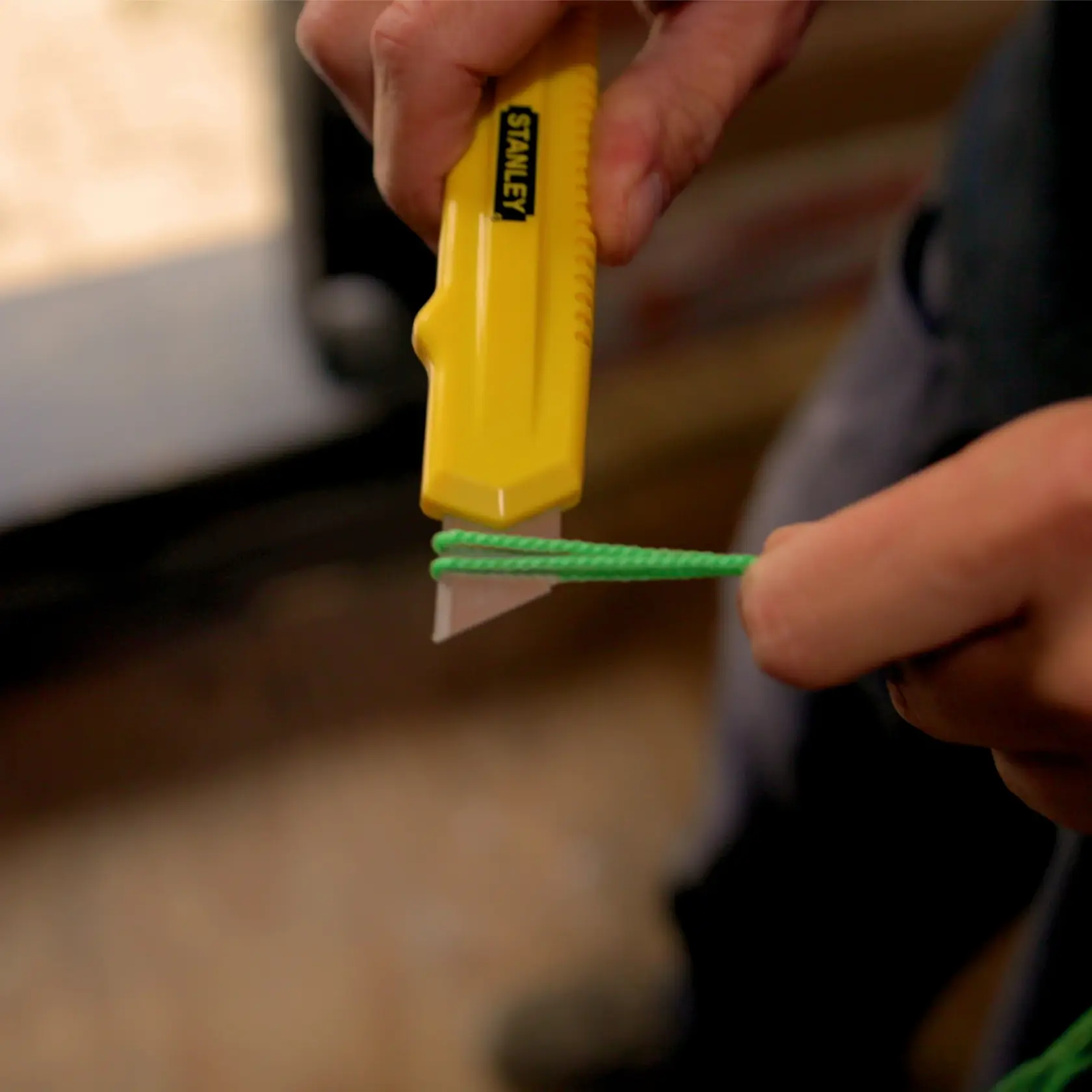STANLEY STMT0-74864 utility knife cutting green cord in close-up photography.