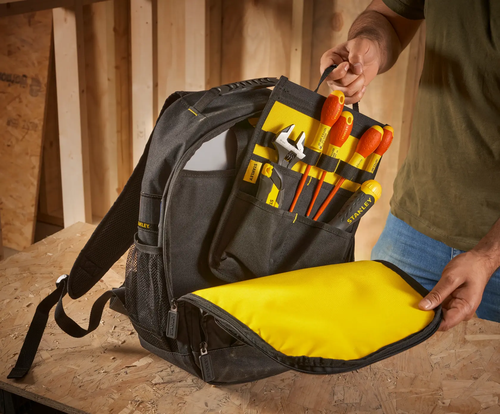 STANLEY STST1-72335 tool backpack with yellow interior, filled with hand tools, shown open on a work surface.