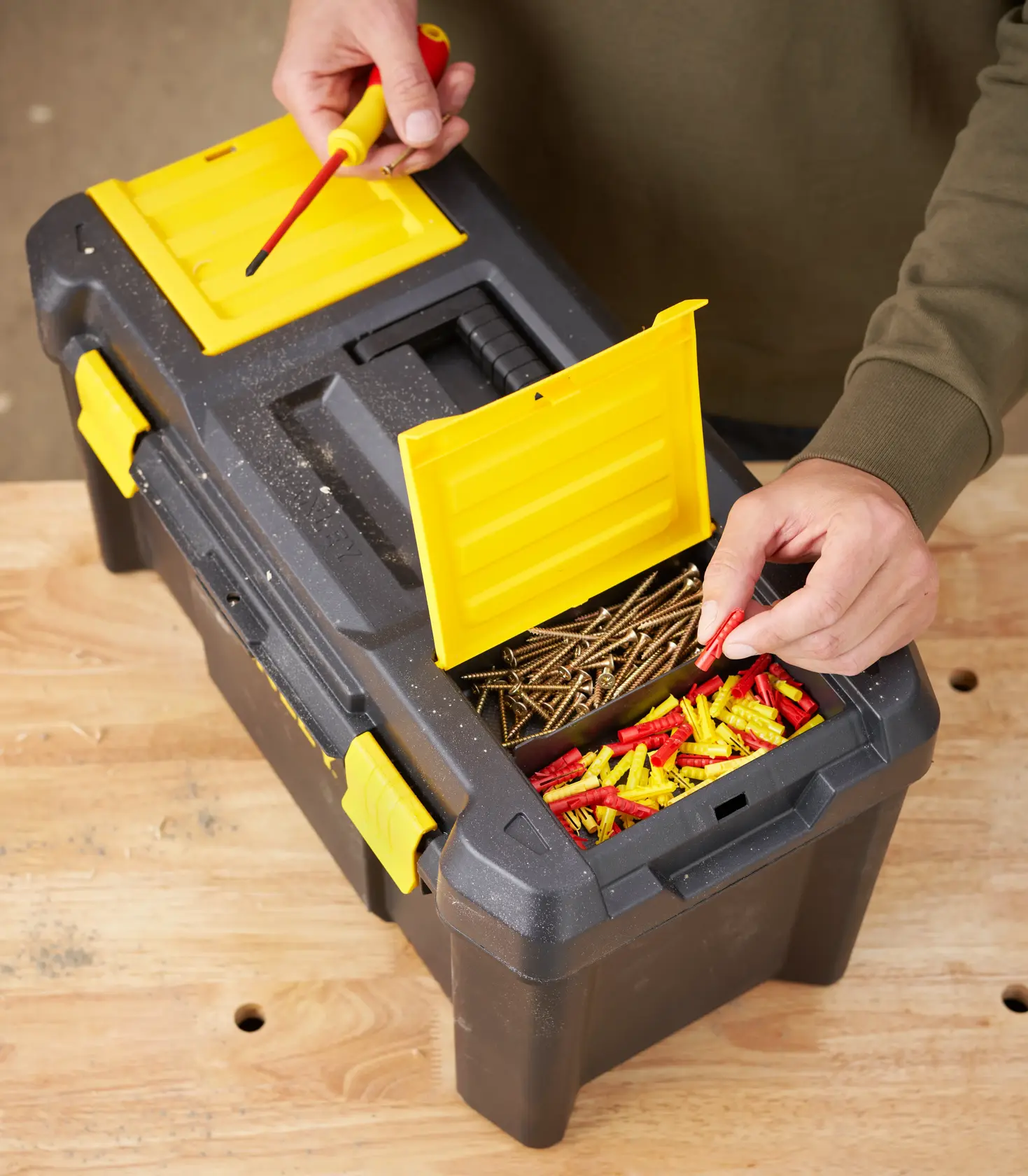 STANLEY STST1-75520 black and yellow toolbox on table, open top compartments with screws and wall plugs, top view.