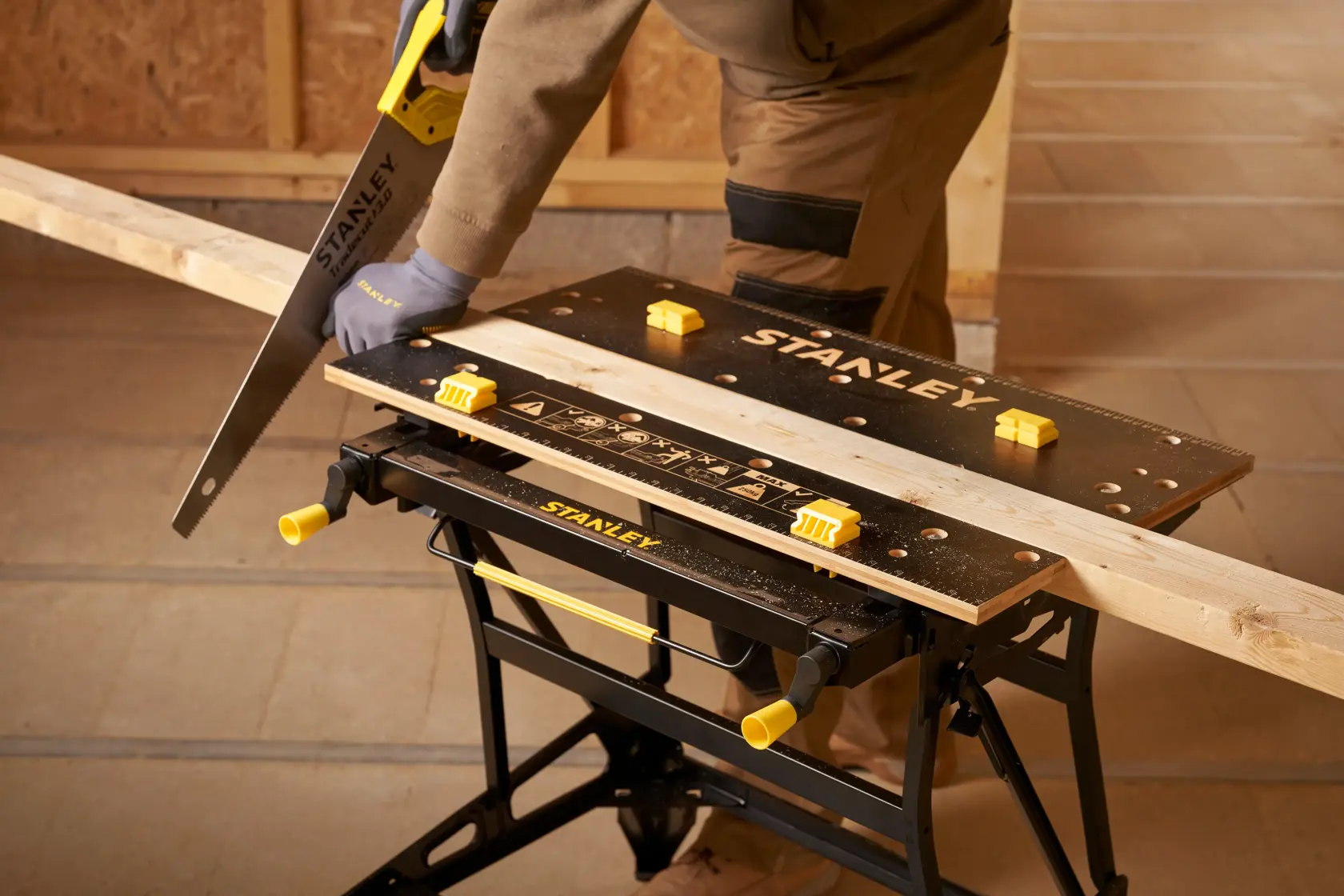 Stanley STST83800-1 workbench with wood plank, handsaw, and person sawing in workshop. Photography product.