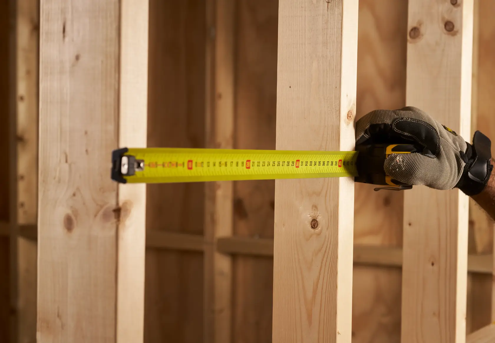 STANLEY XTHT0-33671 tape measure extended, measuring wooden studs with gloved hand during construction.